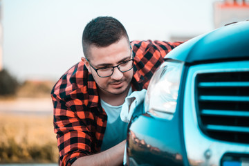 Close up, shoot of a young man carefully polishing his car with a microfiber cloth