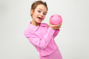 girl in a pink suit holds a piggy bank on a white background with copy space