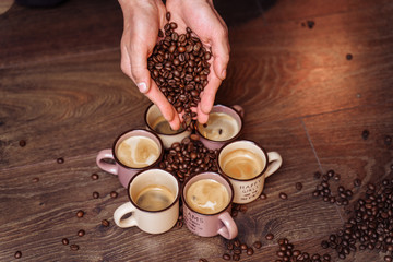 Close-up of the hands of a girl who sprinkles roasted coffee beans to the floor. On the floor there are cups of freshly brewed espresso and a bag of coffee