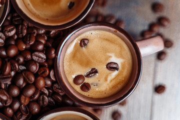 Coffee cup and coffee beans on a wooden background. View from above. Brown background. Close up. Cups with espresso standing on wooden floor, surrounding by roasted beans
