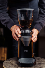 Closeup of a black stylish coffee grinder. Barman holding hands on coffee grinder, preparing to grind fresh, aromatic coffee beans