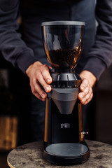 Fototapeta na wymiar Closeup of a black stylish coffee grinder. Barman holding hands on coffee grinder, preparing to grind fresh, aromatic coffee beans