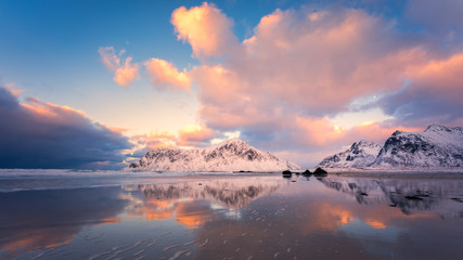 Colorful sky reflected in the water on the beach with snowcapped mountain in the background.