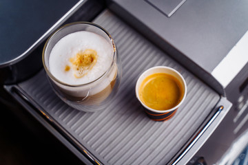 a cup of cappuccino and a cup of espresso are standing on top of an office coffee machine. Inexpensive, simple coffee machine model makes delicious coffee with milk and natural custard americano