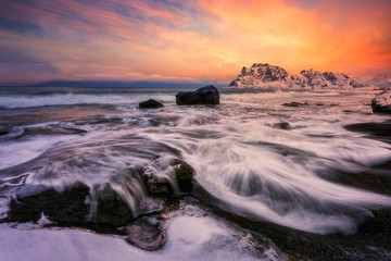 Fototapeta na wymiar Dramatic sunset at beach, with waves washing over coastal rocks.