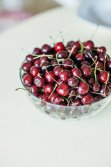 Appetizing ripe juicy cherries in a transparent bowl on the table. A photo with a blurred background.
