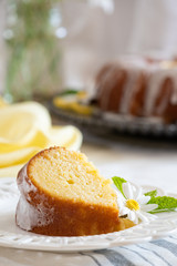 A slice of moist Lemon Ricotta Bundt Cake on a white decorative plate with a daisy and mint leaf garnish.