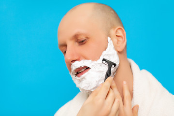 Man in the bathroom shaves his beard with a razor