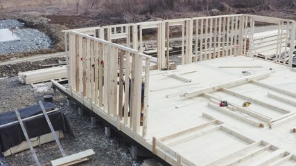 Aerial zooming out view of builders team lifting the wooden wall on the place. Residential frame house under construction