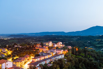 Fototapeta na wymiar Chiusi town village at night in Tuscany, Italy with illuminated lights on streets and rooftop houses on mountain countryside and rolling hills