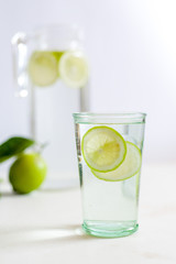 Closeup glass of warm water with lime with a jug and whole fresh lime on the background 