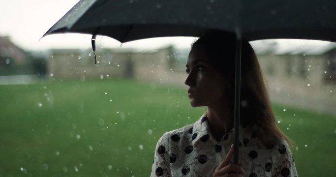 portrait of attractive girl standing under black umbrella during heavy rain. bad rainy weather.