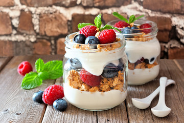 Blueberry and raspberry parfaits in mason jars. Side view against a rustic brick background.