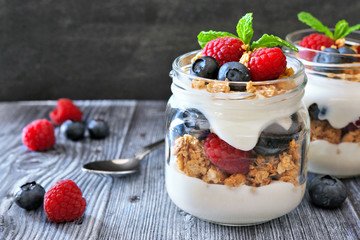 Healthy blueberry and raspberry parfaits in mason jars. Close up table scene on dark rustic background.