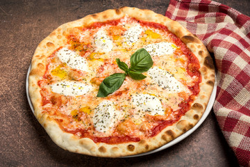 Pizza margarita with cheese, tomato and basil on plate, brown background, top view