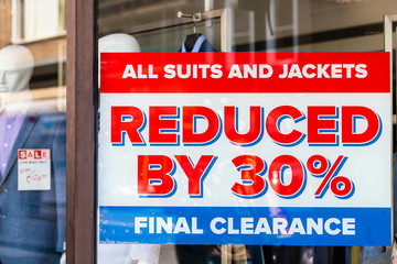 Shopping mall department men's clothing fashion store shop storefront sign closeup of sale price reduction clearance on glass window closeup exterior with mannequin and clothes