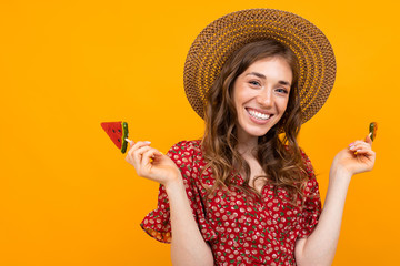 girl in a straw hat and a red summer dress with candy in hand on a yellow isolated background