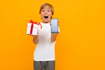 Cute little boy in t-shirt and trousers holds a box with gift himself isolated on yellow background