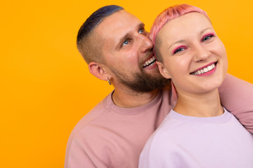 Unusual pretty woman with short pink hair and tattoo enjoys life with her boyfriend isolated on orange background