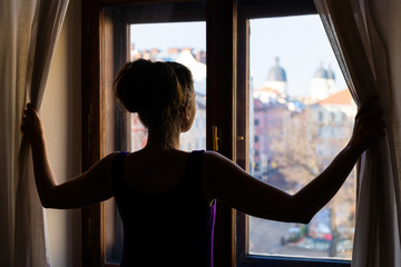 Woman back opening curtains looking from apartment room glass window with view of Lviv, Ukraine old...