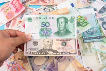 Man Hand holding Bank Note of YUAN RMB and USD Dollar with World banknotes collection mixed on table, top view. Business and finance concept.