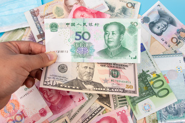 Obraz premium Man Hand holding Bank Note of YUAN RMB and USD Dollar with World banknotes collection mixed on table, top view. Business and finance concept.