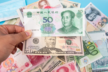Man Hand holding Bank Note of YUAN RMB and USD Dollar with World banknotes collection mixed on table, top view. Business and finance concept.