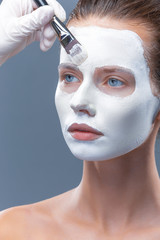 Beautiful girl is applied a white cosmetic mask from black dots. Isolate, studio.