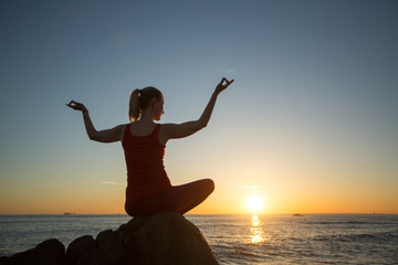 Silhouette of woman doing yoga on the sea beach during sunset.