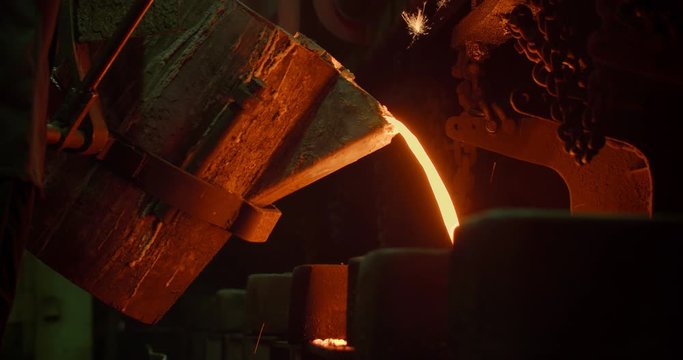 Room for the manufacture of metal products by casting. Casting shop for gassified models. The molten metal is poured from the induction furnace into the ladle. Sparks of hot metal fly apart. Close-up.