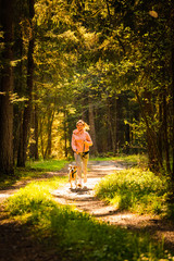 Young woman and dog running together on country in forest. Cheerful female exercising outdoor with her pet.