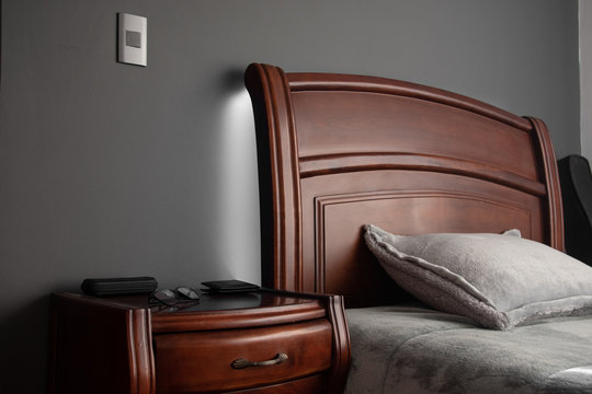 Cama de madera con cobija gris y fondo gris con luces 