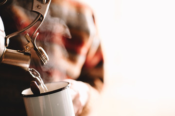 Man pouring boiling water from kettle in mug preparing coffee or tea at home