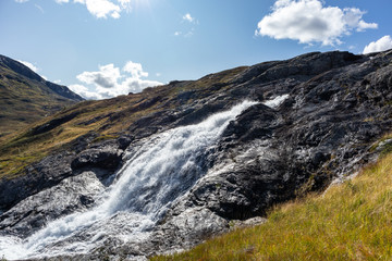 Sunny white scenic norwegian powerful river cascade waterfall with dark rocks and bright blue sky. Nature travel clean falling water landscape