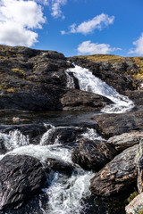 Sunny white scenic norwegian powerful river cascade waterfall with dark rocks and bright blue sky. Nature travel clean falling water vertical landscape