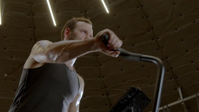 low-angle shot of muscular athlete workout air bike cardio in a dark gym 