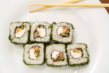 Rolls with salmon and dill on a white plate with chopsticks.
