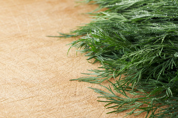 A bunch of fresh dill with small drops of water on a wooden cutting board