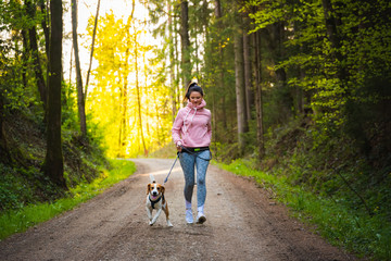 Young woman and dog running together on country in forest. Cheerful female exercising outdoor with her pet.