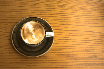 close up of a cup of cappuccino with art foam design on a yellow wooden table in a cosy cafe