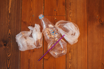 Disposable water bottles, straws and bag, disposable plastic products, on wooden background. The concept of protecting the environment from plastic waste contamination. 

