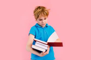 Blonde boy in t-shirt reading a book thirsty for knowledge on pink background.