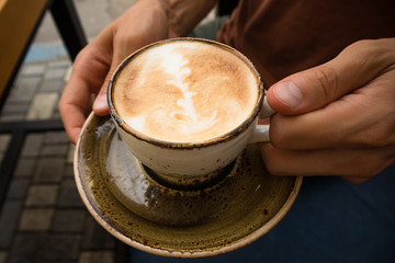 a young handsome man is sitting  in a cafe with friends and drinking hot cappuccino ,relaxing, close up of a cup