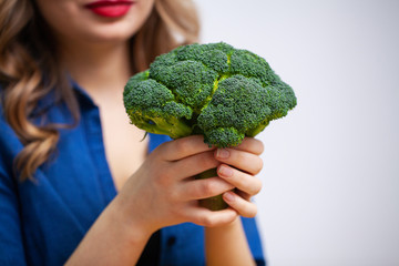 Woman at a table holding a broccoli on white background