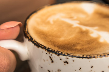 CLose up of a cup with hot cappuccino in girls hand in a cosy cafe 