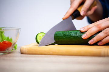 Closeup of woman slices cucumber for fresh salad