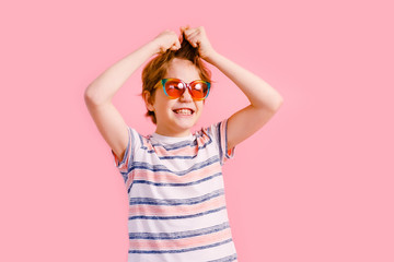 Emotional blonde teen boy in sparkle sunglasses laughing to camera on pink background