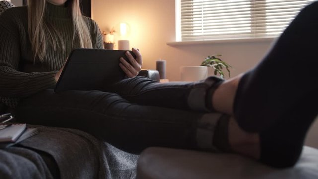 Woman Using a Digital Tablet Sat Down On The Couch in The Evening