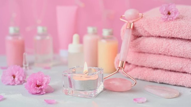 rose quartz roller at pink folded towels and burning candle against various bottles with beauty acids close view