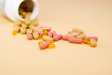 Omega-z, yellow and pink capsules with medicines next to a white bottle of drugs. Light orange background